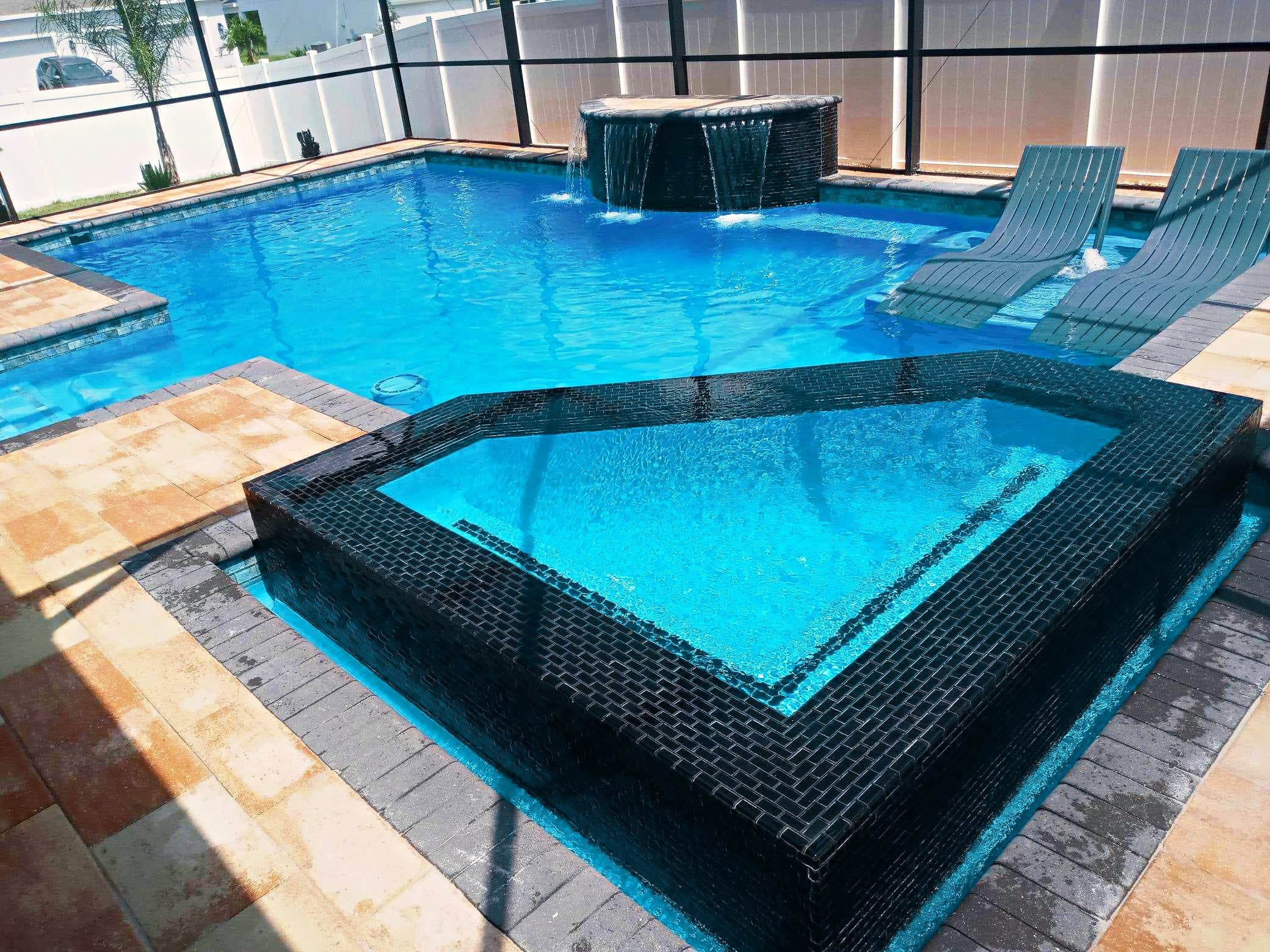 Piscina con jacuzzi elevado y azulejo oscuro terminada por D&J