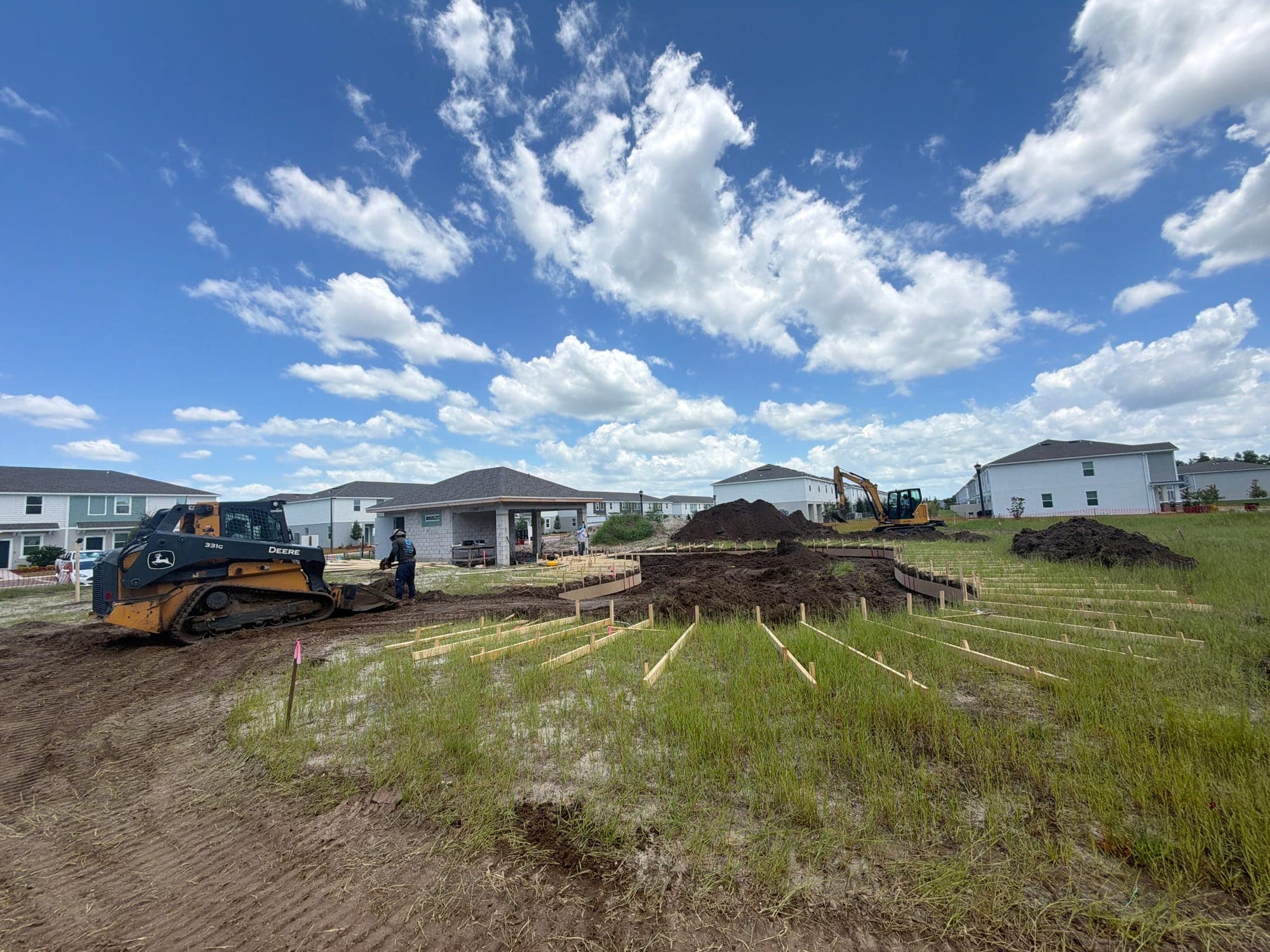 A new pool layout staked out on a lot, with a loader and an excavator on site