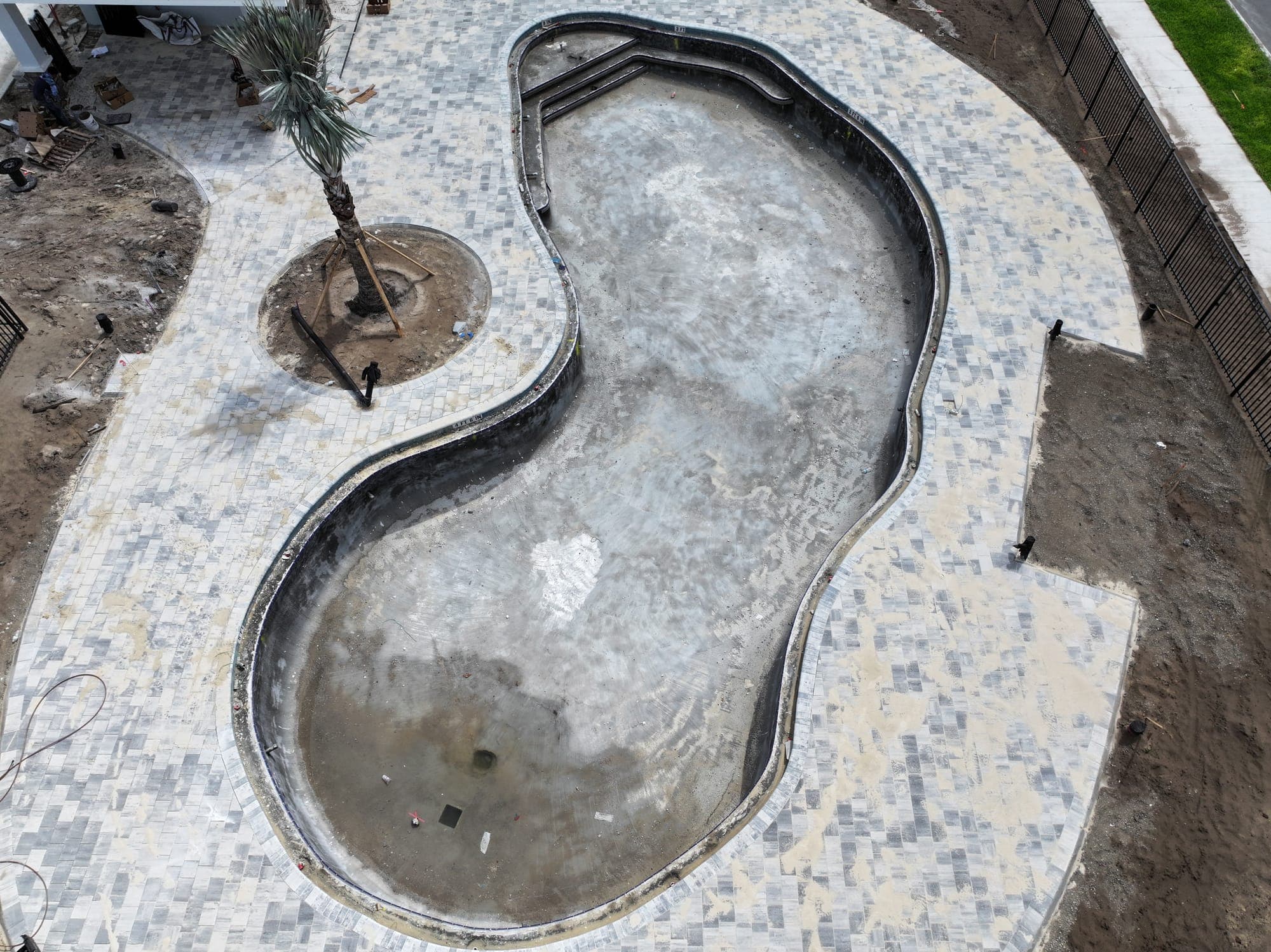 Vista aérea del casco de concreto de una piscina nueva de forma libre, rodeado de adoquines