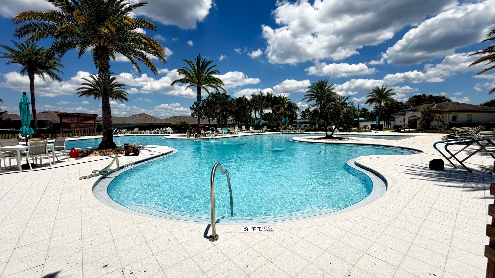 Piscina grande de forma libre con palmeras y pasamanos en la entrada