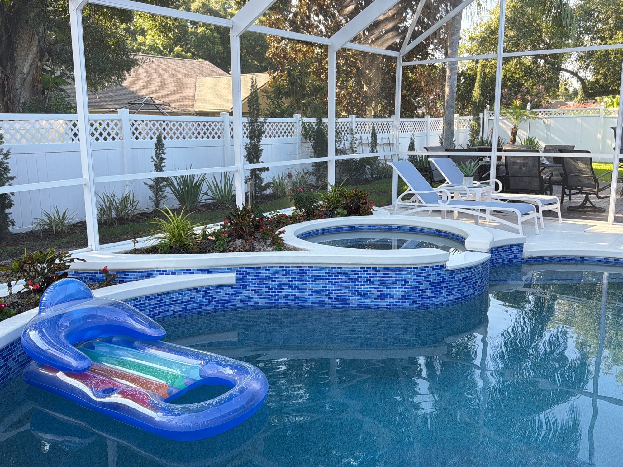 Spa elevado con azulejo de vidrio azul junto a una piscina bajo screen
