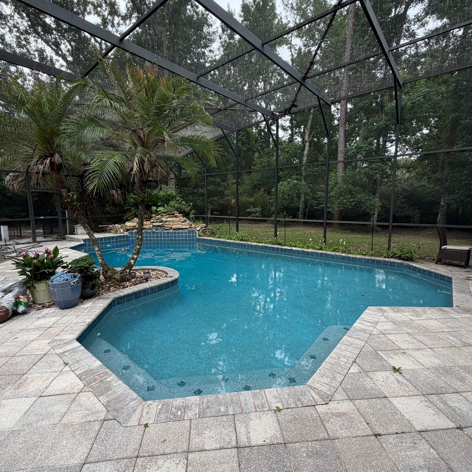 Piscina bajo screen con cascada de roca y terraza de adoquines