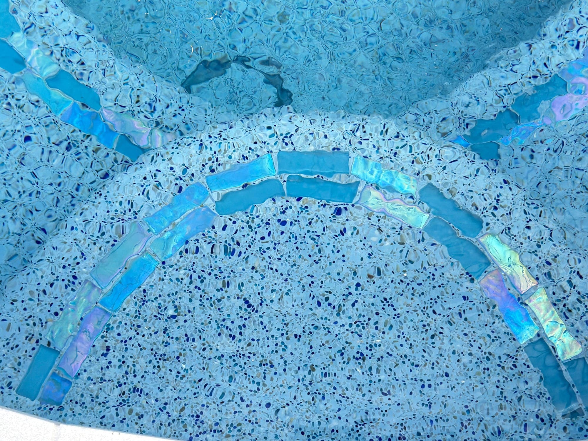 Franjas de azulejo de vidrio iridiscente sobre un acabado de piedrita azul