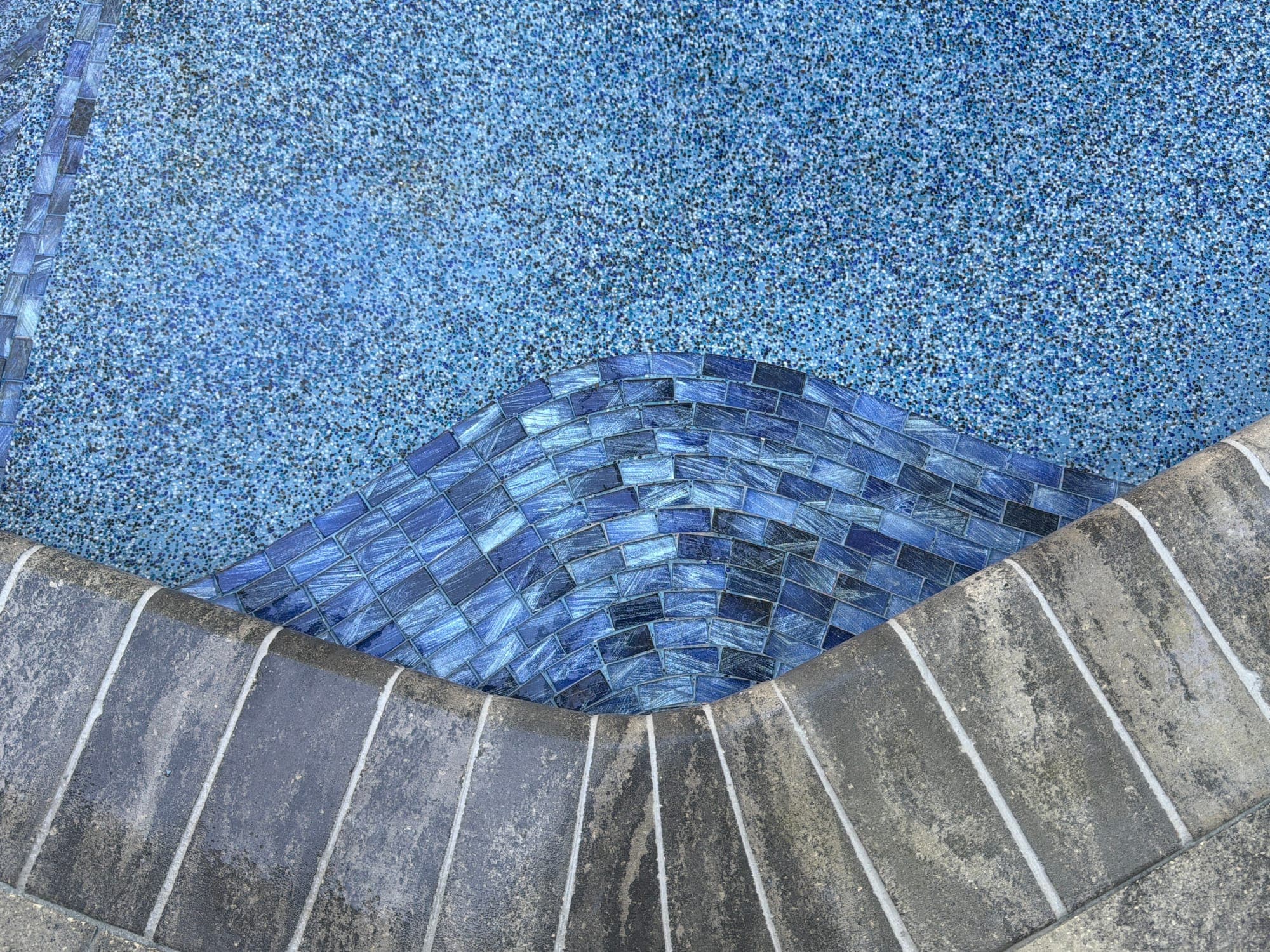 Azulejo de vidrio azul en una esquina de la piscina junto a un acabado de piedrita