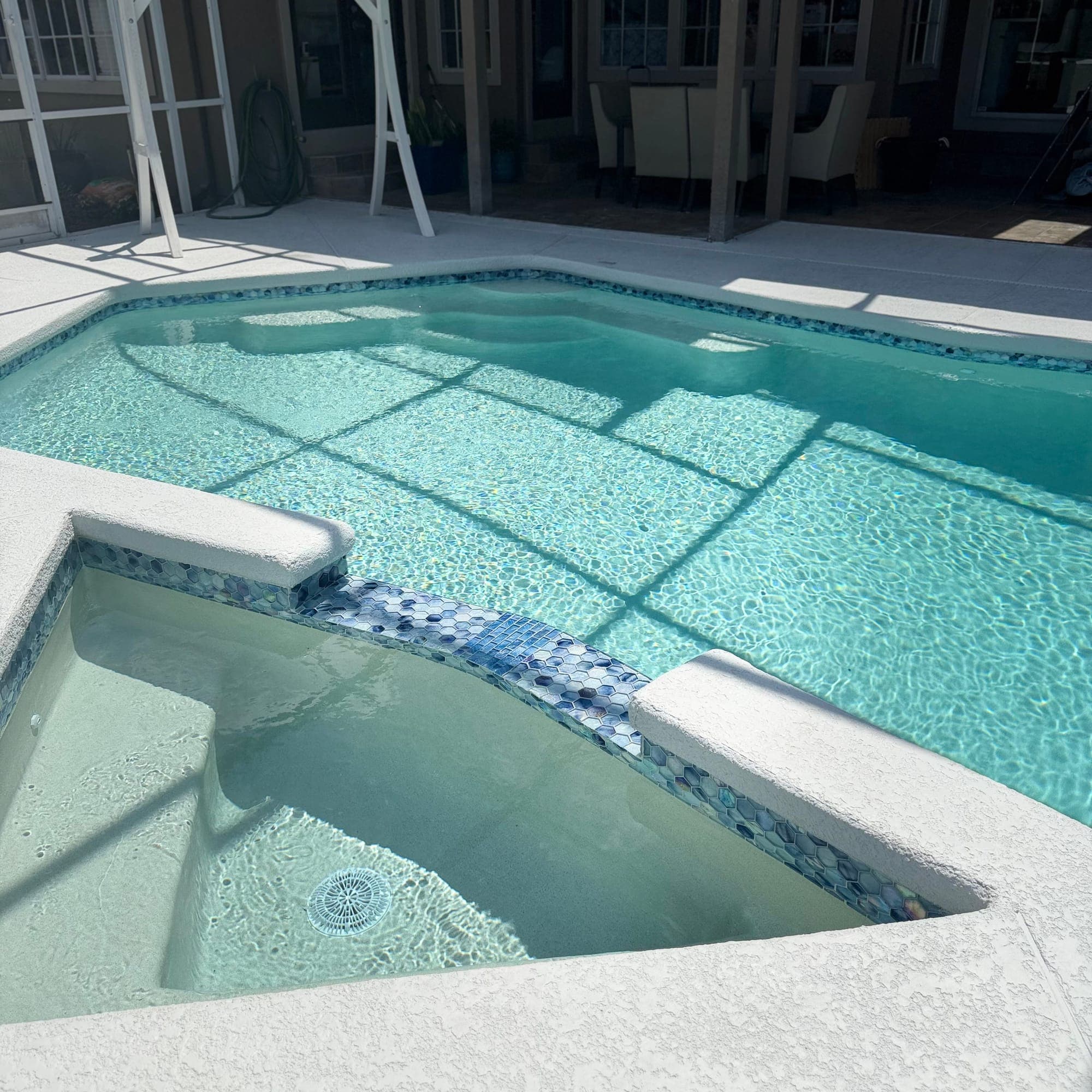 Desborde del spa con mosaico de vidrio junto a una piscina con screen
