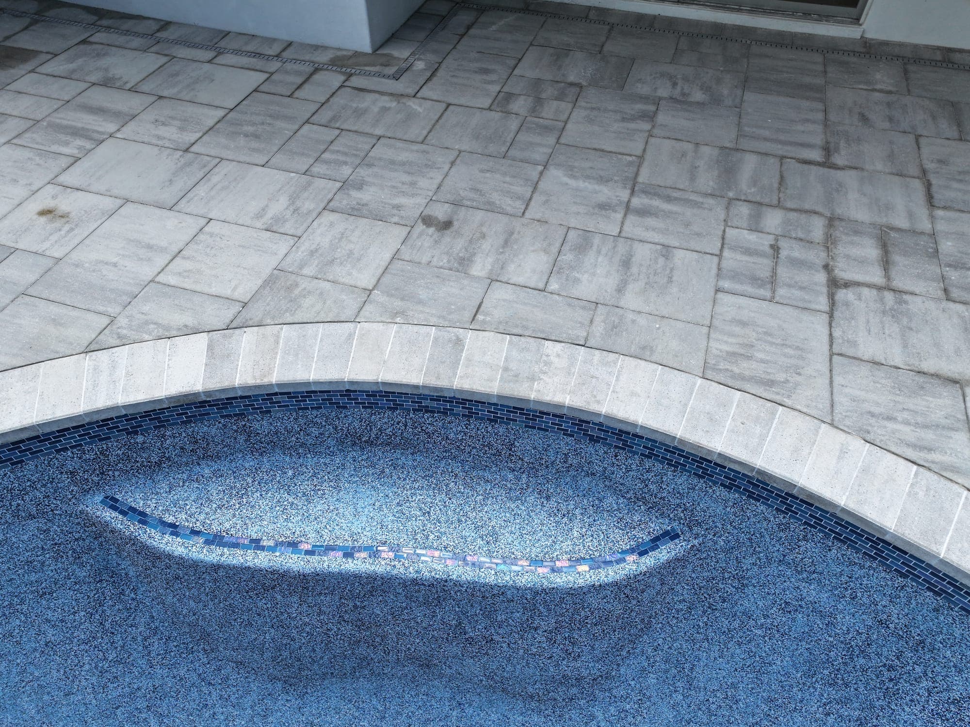 Close-up of new glass tile on the edge of a pool bench, next to the new blue finish
