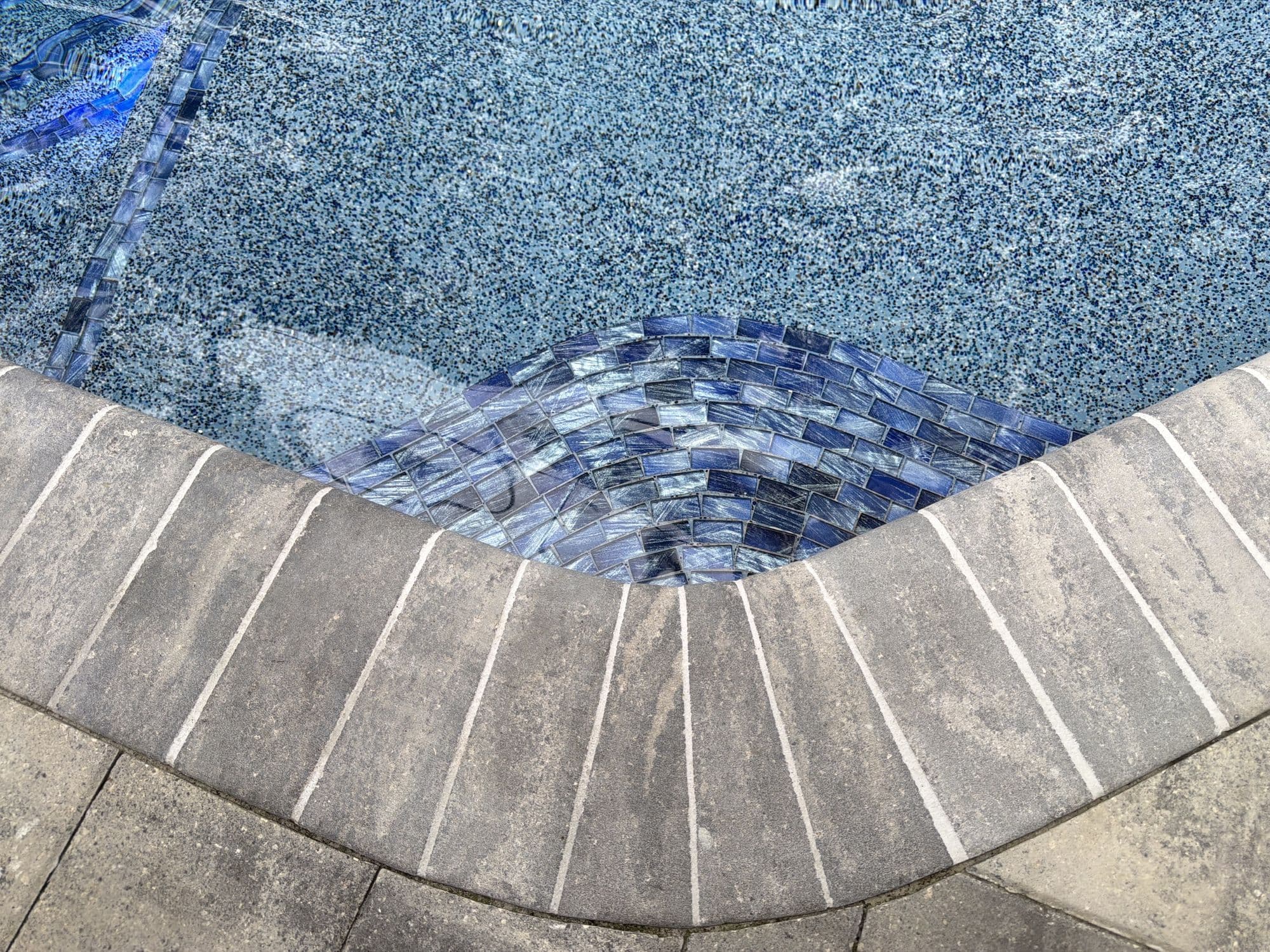 Detalle de un acabado de pebble y azulejo de vidrio en la línea de agua